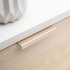 a white vase sitting on top of a wooden counter next to a drawer with gold handles