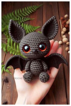 a small crocheted bat sitting on top of a person's hand next to some nuts