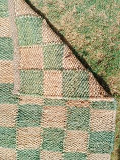 a green and brown checkered blanket laying on top of the ground next to grass