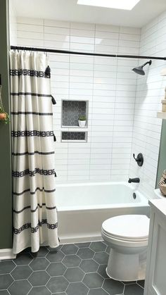 a white toilet sitting next to a bath tub under a bathroom window covered in black and white shower curtains