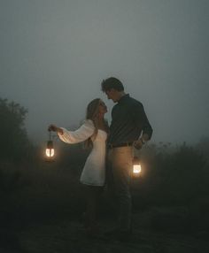 a man and woman standing in the fog holding lantern lights up to their foreheads