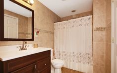 a white toilet sitting under a bathroom mirror next to a sink and a shower curtain