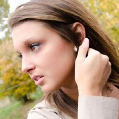 a young woman with ear piercings on her ears looking off into the distance while standing in front of some trees