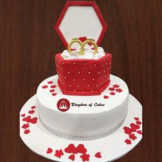 a wedding cake decorated with red and white frosting, two gold rings on top