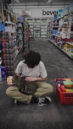 a person sitting on the floor with a cat in front of them and some shelves