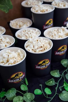 there are many cups with popcorn in them on the table next to some green leaves