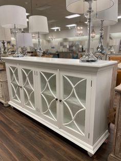 a white cabinet with two lamps on top and some chairs in the background at a furniture store