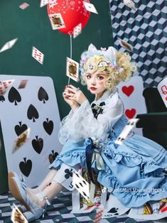 a woman in a blue dress holding a red balloon and playing cards on a black and white checkered floor