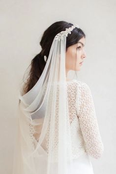 a woman wearing a white veil and wedding dress is standing in front of a wall