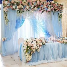 a table set up with blue drapes and flowers