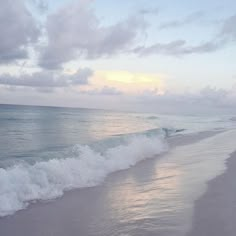 the ocean waves are rolling in on the shore line at sunset or sunrise, as seen from an empty beach