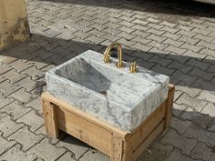 a white marble sink sitting on top of a wooden stand next to a brick sidewalk