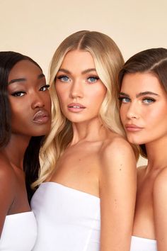 three beautiful women in white dresses posing for the camera with their arms around each other