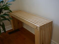 a wooden bench next to a potted plant in a room with hard wood flooring