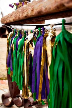 some tassels are hanging from a wooden pole with green, purple and gold ribbons