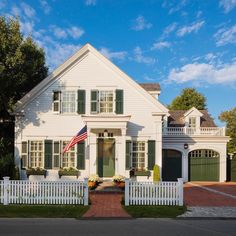 a large white house with green shutters and a flag on the front door is shown