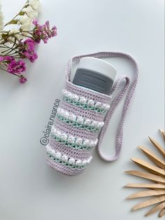 a crocheted cell phone case sitting on top of a table next to flowers