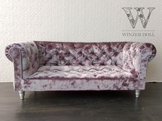 a purple velvet couch sitting on top of a wooden floor next to a white wall