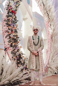 a man standing in front of an arch with flowers and feathers on it's sides