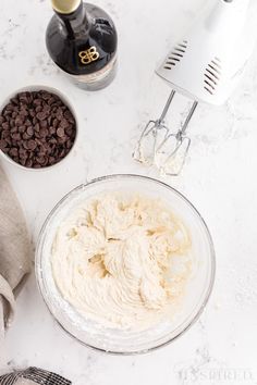 ingredients to make chocolate chip cookies on a white counter with a blender and mixer in the background