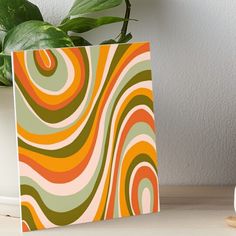 an orange and green swirl pattern on a white background art boarder next to a potted plant