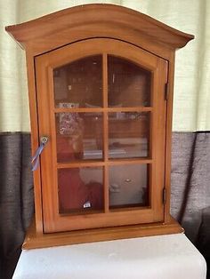 an old wooden china cabinet with glass doors and white cushion on the bottom, in front of a curtained window