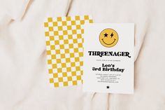 there is a yellow and white birthday card with a smiley face on it, next to a checkered sheet