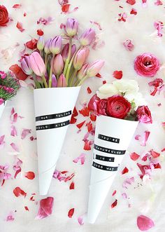 three paper cones with flowers in them on a bed of rose petals and petals scattered around