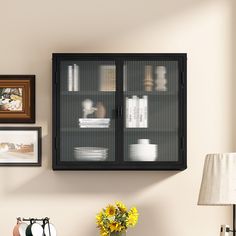 a black cabinet with glass doors next to a lamp and pictures on the wall