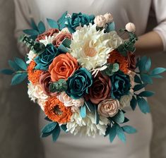 a bridal bouquet with orange, white and blue flowers is held by a woman