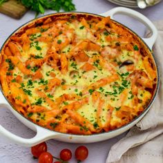 a casserole dish with cheese, tomatoes and parsley on the table next to it