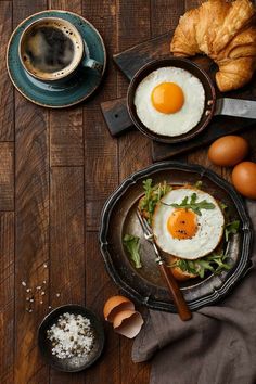 two eggs are sitting on top of a plate next to croissants and coffee