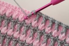 the crochet stitch is being worked on with a pink handled knitting needle in front of it