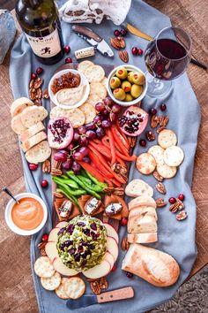 a platter filled with cheese, crackers and fruit next to wine glasses on a table