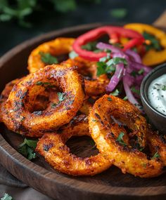 some onion rings are on a wooden plate with dip and veggies in the background