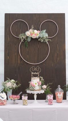 a table topped with lots of cake and desserts next to a wooden sign that says mickey mouse