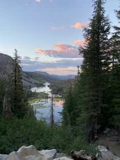 the sun is setting over a lake surrounded by pine trees and mountains in the distance