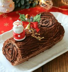 a piece of chocolate cake on a white plate with christmas decorations around it and a santa clause figurine