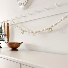 a white dresser topped with a wooden bowl filled with beads and star decorations next to a clock