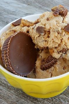 a yellow bowl filled with cookies and chocolates on top of a wooden table next to a cup