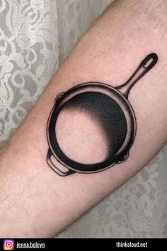 a black and white image of a frying pan tattoo on the left inner arm