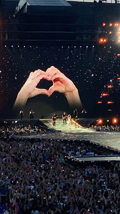 a large crowd at a concert with hands in the shape of a heart on stage