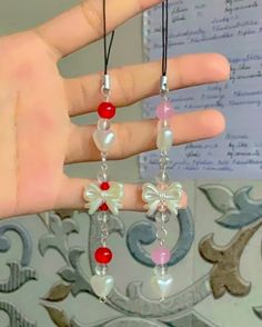 the hand is holding two necklaces with red beads and white flowers on them,