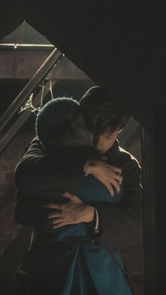 two people hugging each other in front of some stairs and an open door with the light shining on them