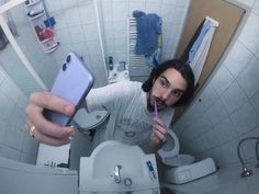 a man taking a selfie in the bathroom while brushing his teeth with an electric toothbrush