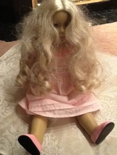 a doll with blonde hair and pink dress sitting on a white doily covered table