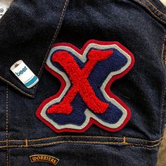 a patch on the back of a jean jacket that says x with red, white and blue letters