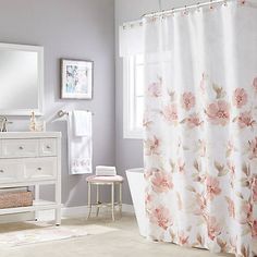 a white bathroom with pink flowers on the shower curtain and vanity, toilet and mirror