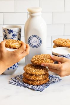 two hands holding oatmeal cookies in front of milk bottles