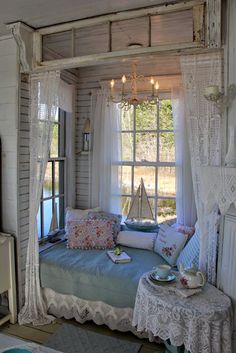 a room with a bed, table and window in it that has curtains on the windowsill